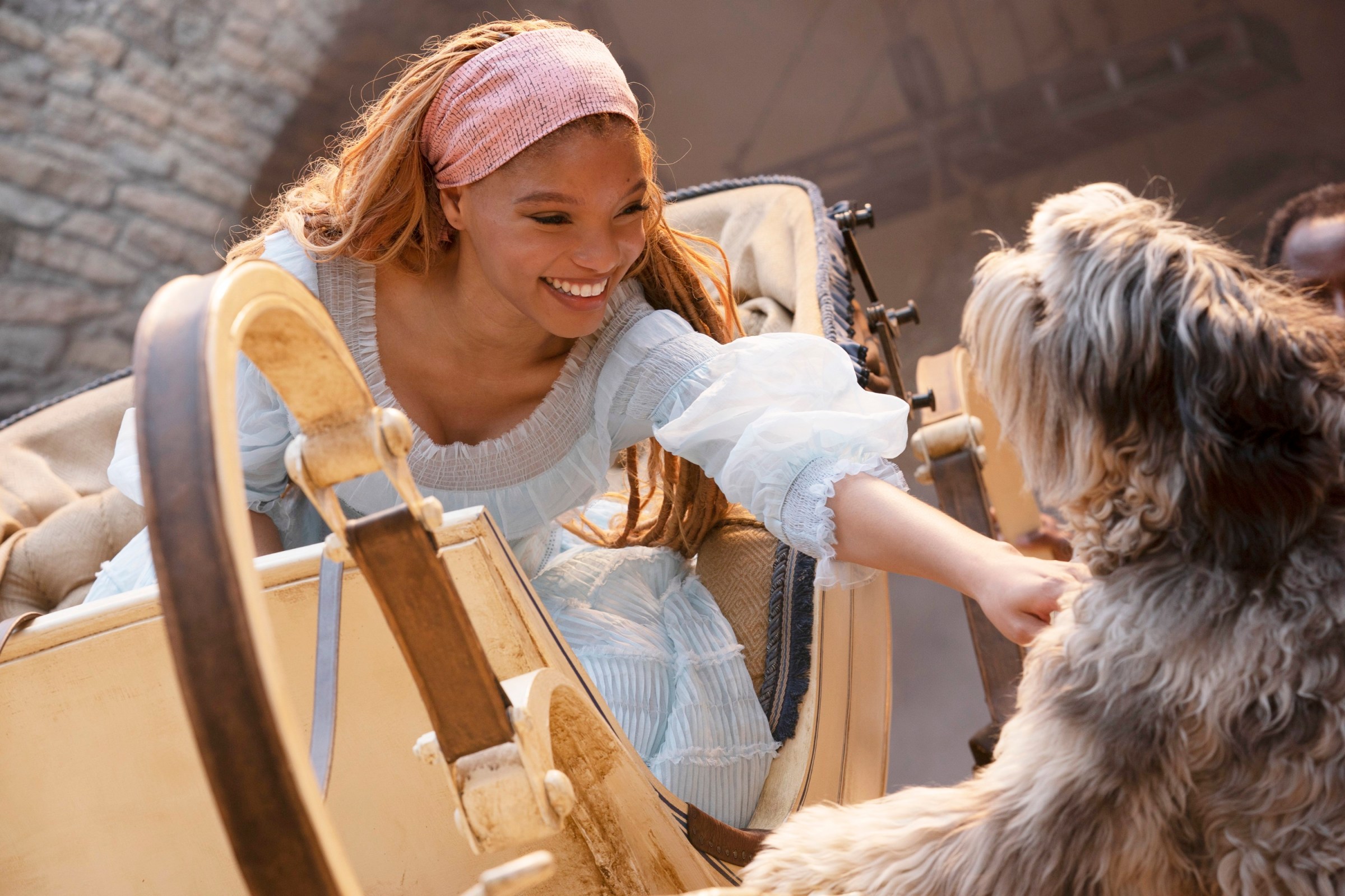 Ariel (Halle Bailey) in a frothy white dress, leaning down from a carriage to pet a dog in Disney’s live-action Little Mermaid