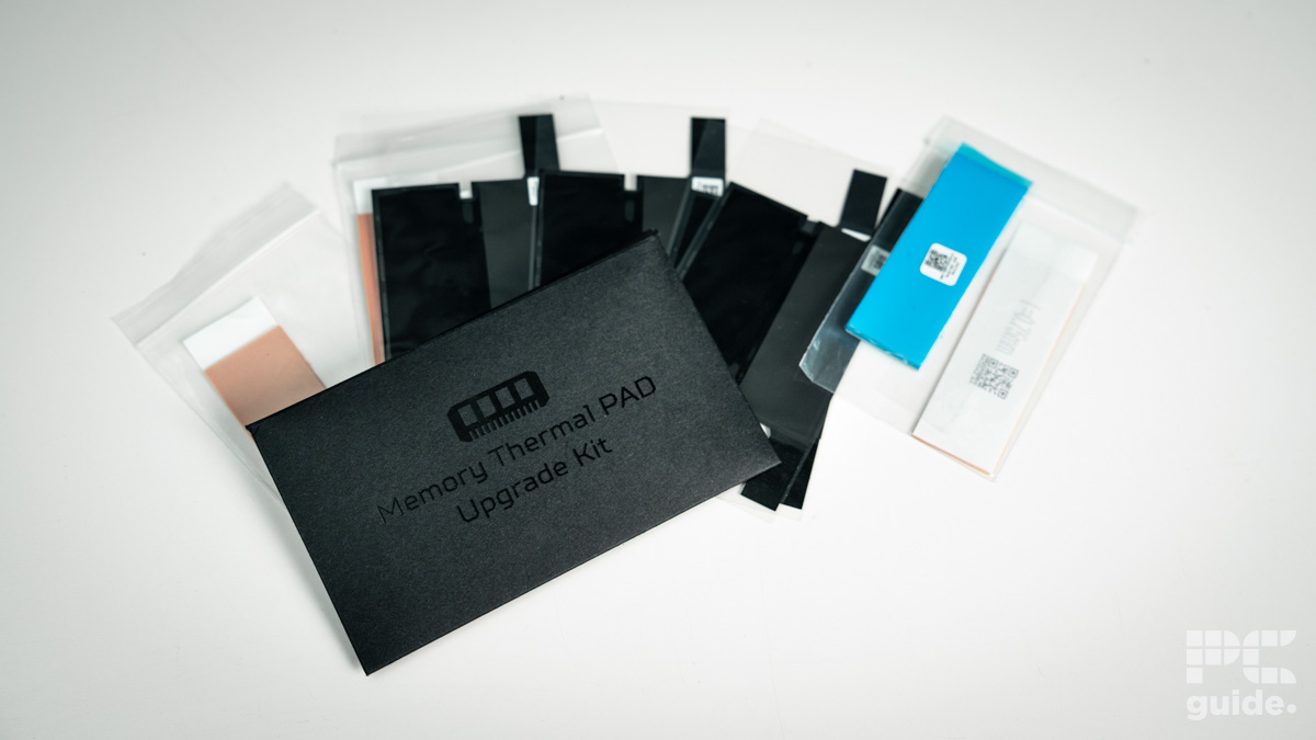 A black small envelope that reads memory thermal PAD upgrade Kit with black lettering too. underneath are a range of thermal padas in black, blue, white, and cream. It sits on a white table.